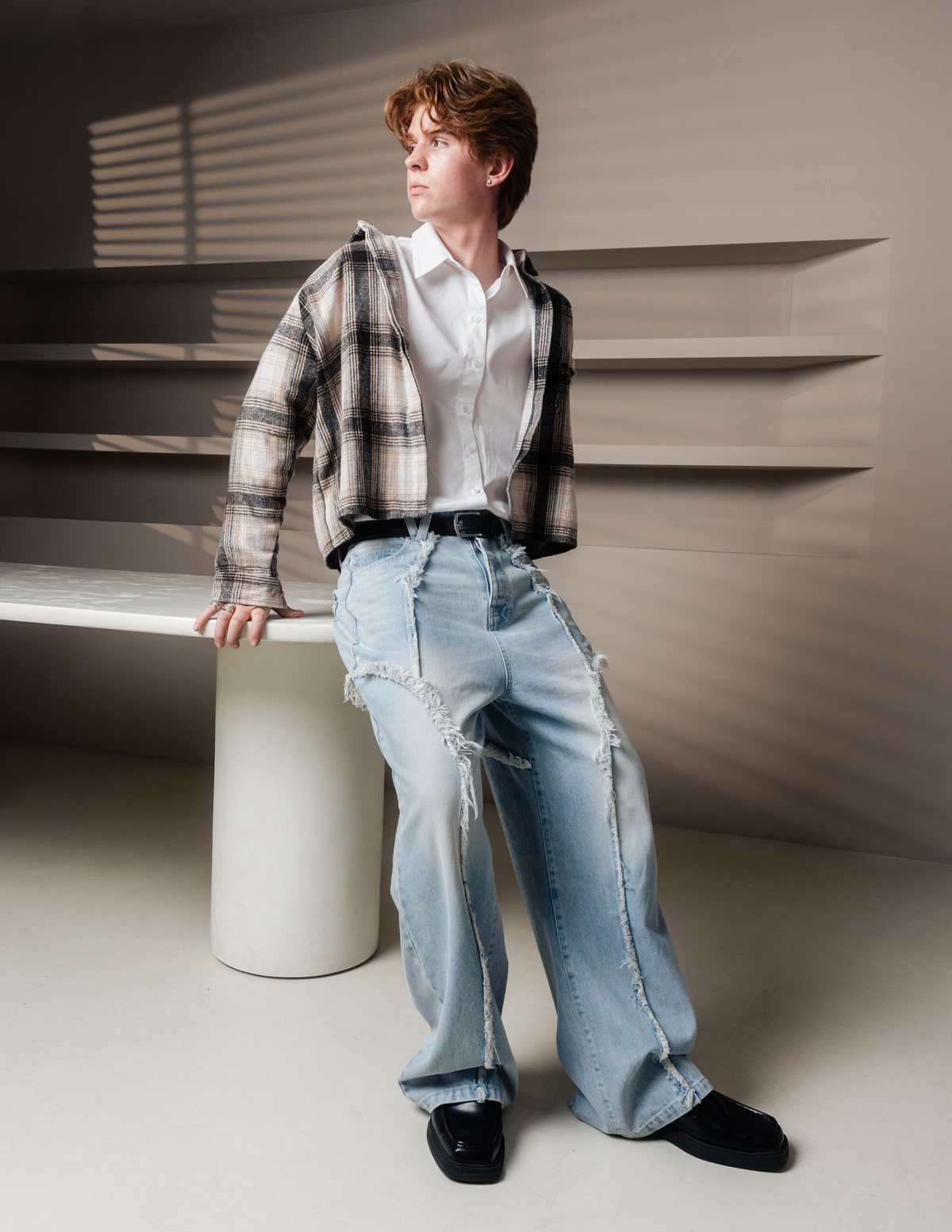 A figure in VERA — plaid shirt over white, Genesis Denim, in soft studio light.